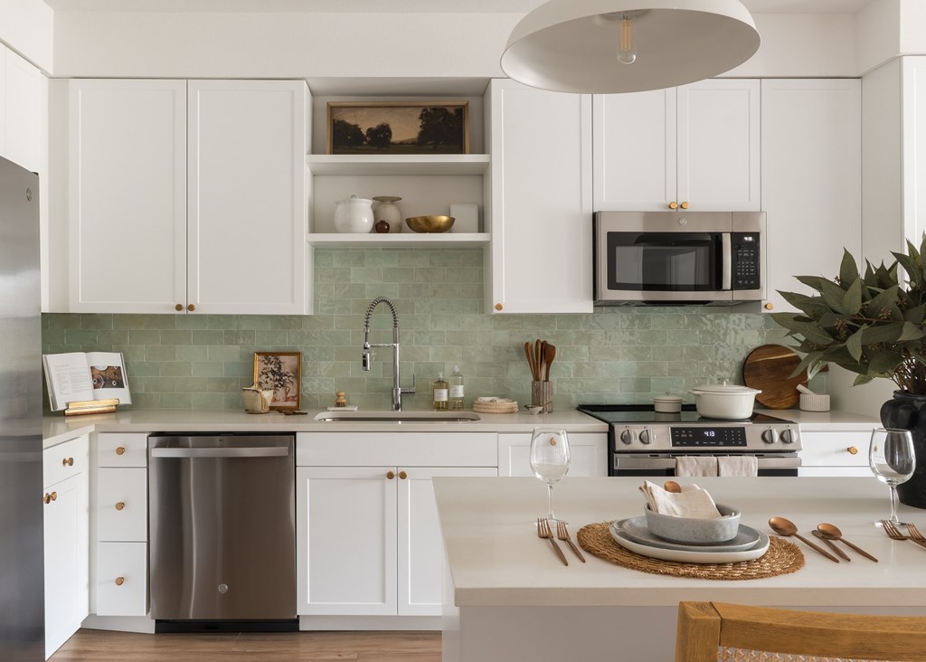 A modern kitchen with white cabinets and a green backsplash.